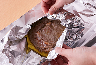 長さ30センチくらいに切ったアルミホイルを2枚重ねて広げ、中央に牛肉をのせて、フライパンに残った油をかけてから全体を包み、3分おく。（アルミホイルを2枚重ねることで大きな肉でもしっかり包め、余熱で火が通る。）