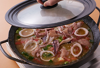 1で用意した2カップ分のスープを入れ、木べらなどでパエリアパンの底から全体をよく混ぜる。米を平らにならして、いか、鶏肉を均一に並べ、ローリエを半分に折って加える。ふたをして、沸騰したら弱火にし、ふつふつ小さく煮立つくらいの火加減で12～15分炊く。火を止めてあさりを加え、再びふたをして10分ほど蒸らす。パセリを散らし、レモンを添える。※あさりを入れるときに米が固ければ水大さじ2～3をかけ、ふたをして30秒ほど加熱してから蒸してください。